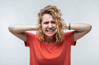 Kafasını tutan, sıradan tişörtlü, kıvırcık saçlı, stresli sarışın bir kız resmi. Duygusal acizlik var. Sorunlar, sürpriz, korku, fobi konsepti. Stüdyo çekimi, beyaz arkaplan.