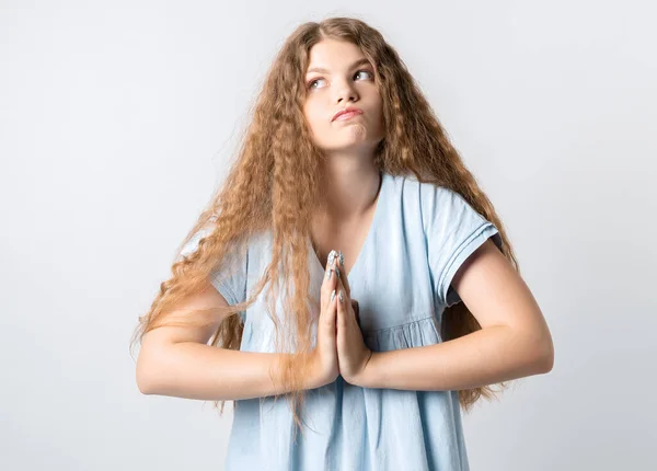 Photo of Pensive European young woman with curly long hair, looking up having pensive expression. Isolated over white background.