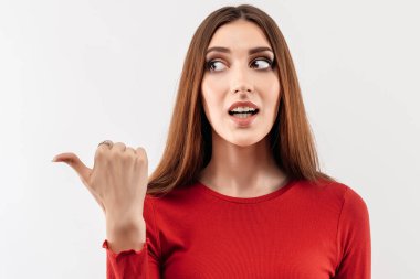 Uzun kestane rengi saçlı, sıradan kırmızı süveter giyen, gülümseyen ve başparmağıyla işaret eden genç bir kadın görüntüsü reklama yer veriyor. Stüdyo çekimi, beyaz arkaplan, izole edilmiş