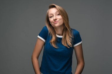 Sarışın, güzel bir kadının stüdyo fotoğrafı. Mavi tişört giyiyor, gizemli bakışlar atıyor. Yasadışı ya da gizlice bir şeyler yapmak istiyor.