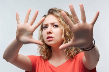 Kıvırcık saçlı, sıradan tişörtlü ciddi sarışın bir kızın görüntüsü aktif olarak kameraya el hareketi yapıyor, elleriyle hareket etmeyi kes. Olmaz, kes şunu. Stüdyo fotoğrafı, beyaz arka plan. İnsan duyguları kavramı