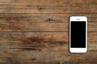 Ahşap masa arkasında boş ekranlı cep telefonu. Eski ahşap döşeme kumaş arka planında akıllı telefon. Üst görünüm, boşluk kopyala