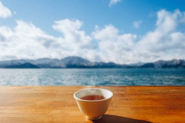 Tahta masada, gölle ve kışın güneş ışığıyla dağların manzarasıyla sıcak bir fincan çay.