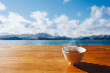 Tahta masada, gölle ve kışın güneş ışığıyla dağların manzarasıyla sıcak bir fincan çay.