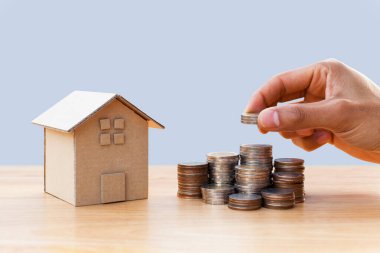 Hand putting money coins to stack of coins with house model and growing plant on row of coin money for finance and banking. Investment and saving concept