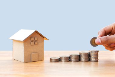 Hand putting money coins to stack of coins with house model and growing plant on row of coin money for finance and banking.