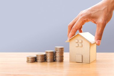 Hand holding house model and money stack on wooden table. Concept for property ladder, mortgage and real estate investment. Investment and business growth concept