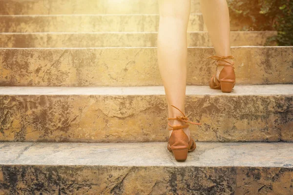 Close up legs of young woman walking stepping up stair in attractions. Feet and leg of young woman wearing brown high going up the stairs outdoors. Alone travel concept