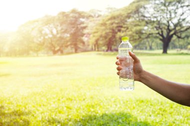 Hand holding drinking water bottle in the park