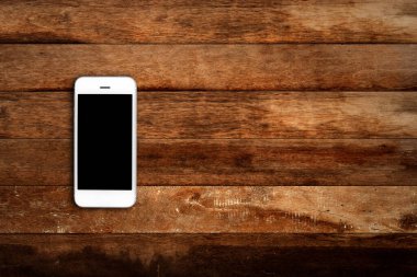 Ahşap masa arkasında boş ekranlı cep telefonu. Eski ahşap döşeme kumaş arka planında akıllı telefon. Üst görünüm, boşluk kopyala