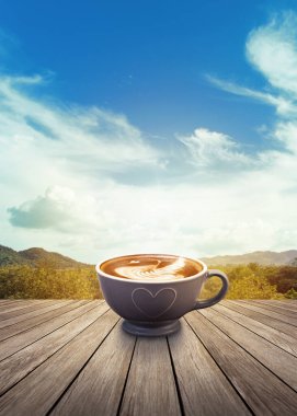 Bir fincan kahve ile ahşap masa üzerinde güzel Latte sanat Sabah manzara dağ ve bulutlu gökyüzü arka planı karşı