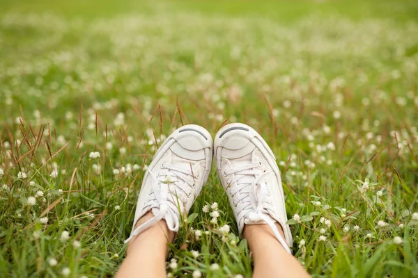Feet in white sneaker on the grass with white flower in the park. Alone travel concept