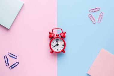 Bir not defteri ataç kırmızı alarm saatli bir pastel pembe ve mavi arka plan düz yatıyordu.