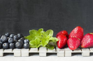 Taze çilek çilek yaban mersini nane kopya alanı metin için bir ahşap stand, gri zemin üzerine.