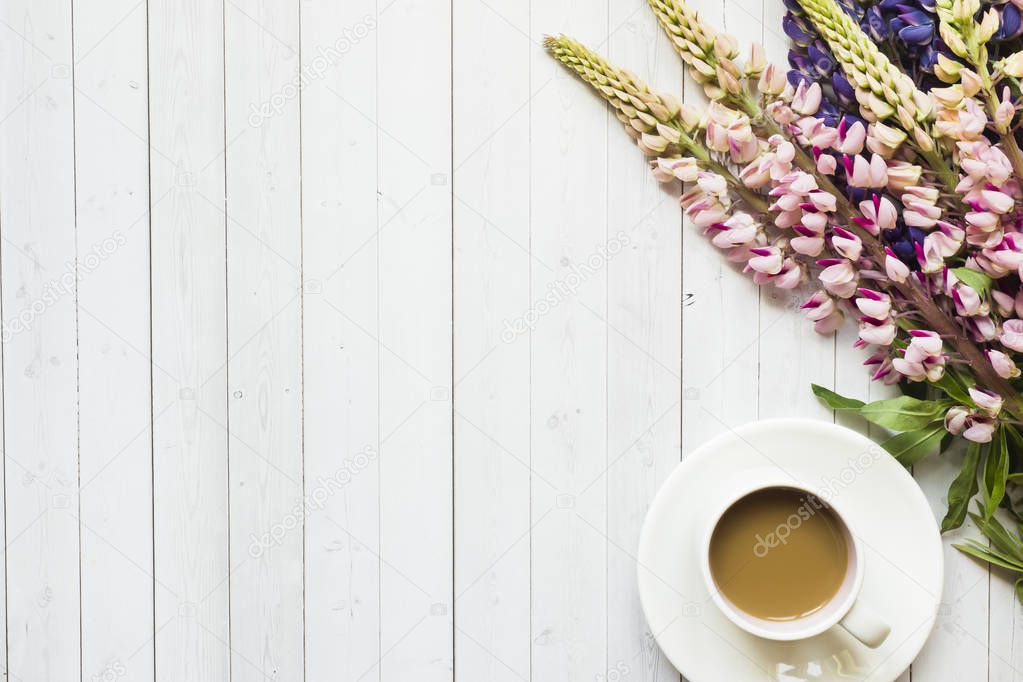 Still life with a Cup of coffee and lupine flowers donut on a light wooden table Copy space