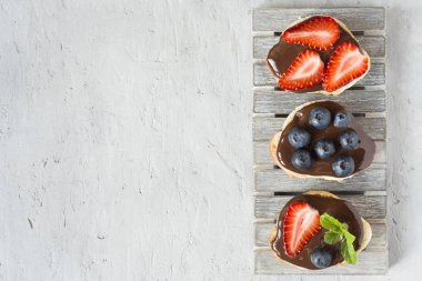 Tost ekmeği ile çikolata yayıldı ve çilek çilek yaban mersini nane gri bir ahşap stand masada. Kopya alanı