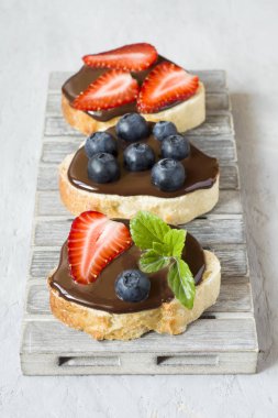 Tost ekmeği ile çikolata yayıldı ve çilek çilek yaban mersini nane bir ahşap stand tabloda gri.