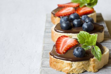 Tost ekmeği ile çikolata yayıldı ve çilek çilek yaban mersini nane gri bir ahşap stand masada. Kopya alanı