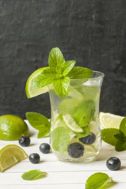 Serinletici içecekler limonata yaz ya da kireç taze nane yaban mersini buzla kokteyl Mojito. Masa lambası, karanlık duvar.