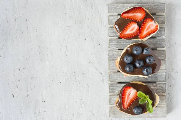 Tost ekmeği ile çikolata yayıldı ve çilek çilek yaban mersini nane gri bir ahşap stand masada. Kopya alanı