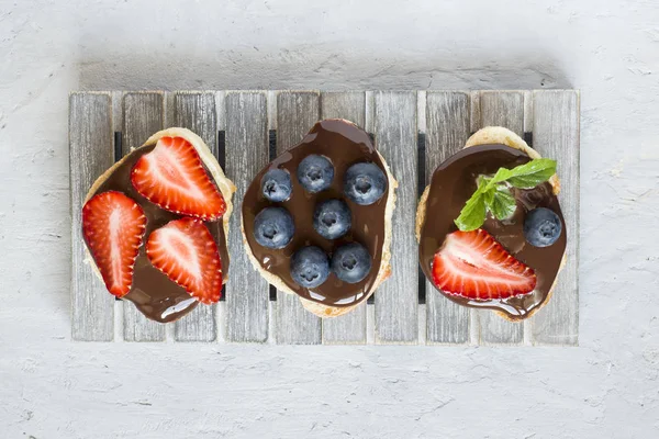 Tost ekmeği ile çikolata yayıldı ve çilek çilek yaban mersini nane bir ahşap stand tabloda gri.