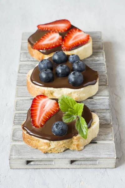 Tost ekmeği ile çikolata yayıldı ve çilek çilek yaban mersini nane bir ahşap stand tabloda gri.