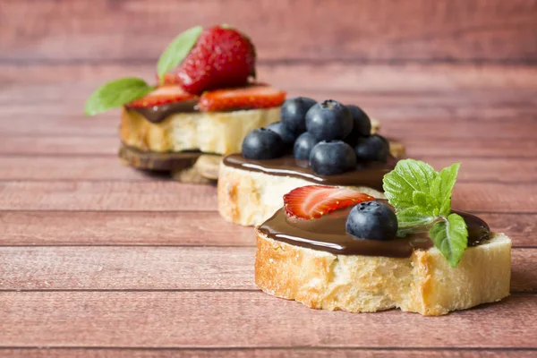 Toast bread with chocolate paste and strawberries blueberries mint on the table. Copy space