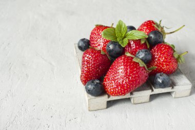 Taze çilek çilek yaban mersini nane kopya alanı metin için bir ahşap stand, gri zemin üzerine.