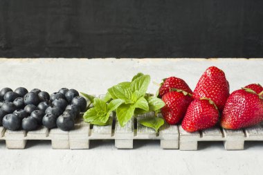 Taze çilek çilek yaban mersini nane kopya alanı metin için bir ahşap stand, gri zemin üzerine.
