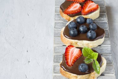 Tost ekmeği ile çikolata yayıldı ve çilek çilek yaban mersini nane bir ahşap stand tabloda gri.