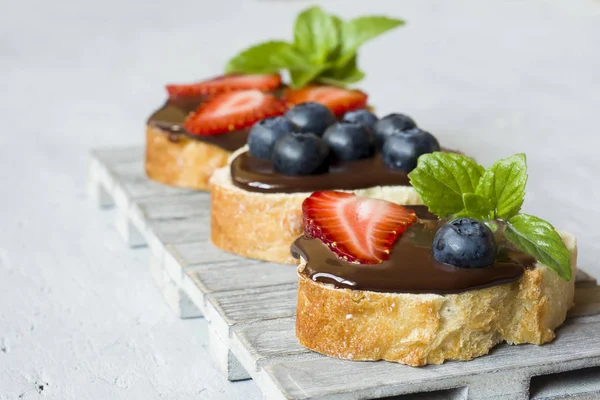 烤面包与巧克力传播和浆果草莓蓝莓薄荷在木立场表灰色 — 图库照片