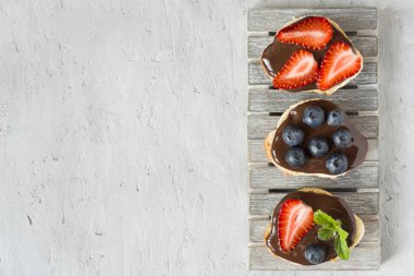 Tost ekmeği ile çikolata yayıldı ve çilek çilek yaban mersini nane bir ahşap stand tabloda gri.