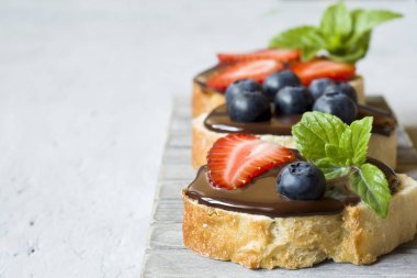 Tost ekmeği ile çikolata yayıldı ve çilek çilek yaban mersini nane bir ahşap stand tabloda gri.