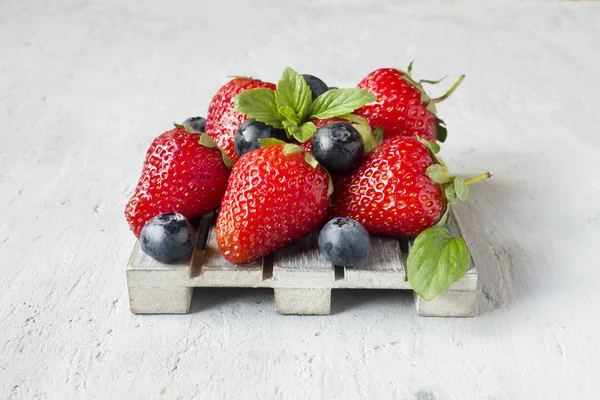 Taze çilek çilek yaban mersini nane kopya alanı metin için bir ahşap stand, gri zemin üzerine.
