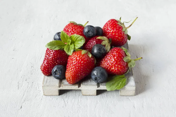 Taze çilek çilek yaban mersini nane kopya alanı metin için bir ahşap stand, gri zemin üzerine.