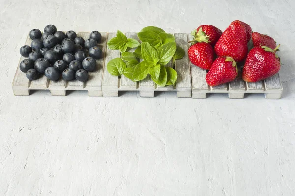 Taze çilek çilek yaban mersini nane kopya alanı metin için bir ahşap stand, gri zemin üzerine.