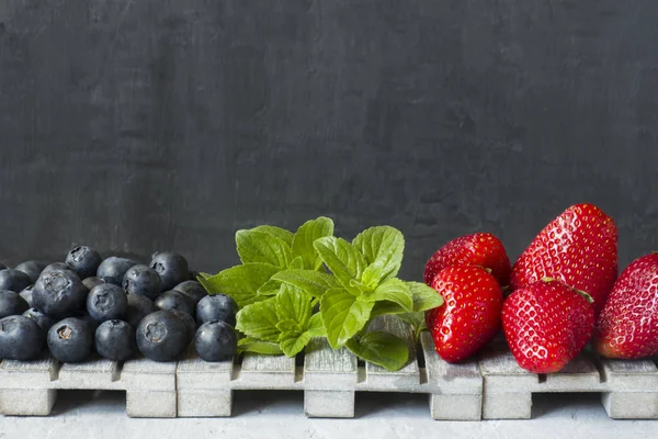 Taze çilek çilek yaban mersini nane kopya alanı metin için bir ahşap stand, gri zemin üzerine.