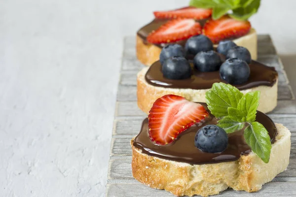 Tost ekmeği ile çikolata yayıldı ve çilek çilek yaban mersini nane bir ahşap stand tabloda gri.
