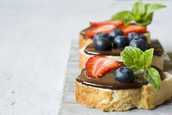 烤面包与巧克力传播和浆果草莓蓝莓薄荷在木立场表灰色 — 图库照片