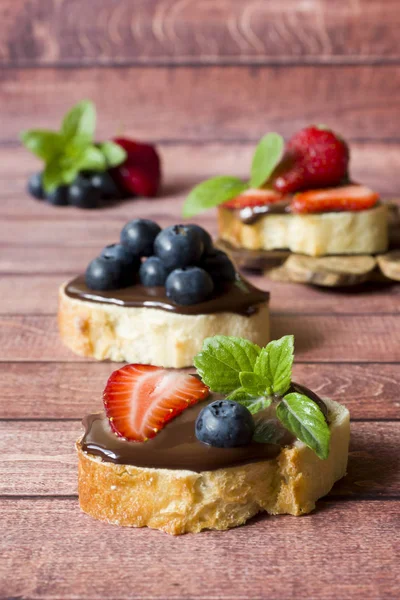 Toast bread with chocolate paste and strawberries blueberries mint on the table. Copy space