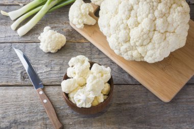 Taze organik karnabahar, ahşap zemin üzerine yeşil soğan ve bıçak ile parçalar halinde kesilmiş.