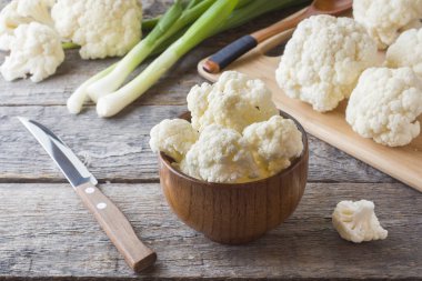 Taze organik karnabahar, ahşap zemin üzerine yeşil soğan ve bıçak ile parçalar halinde kesilmiş.