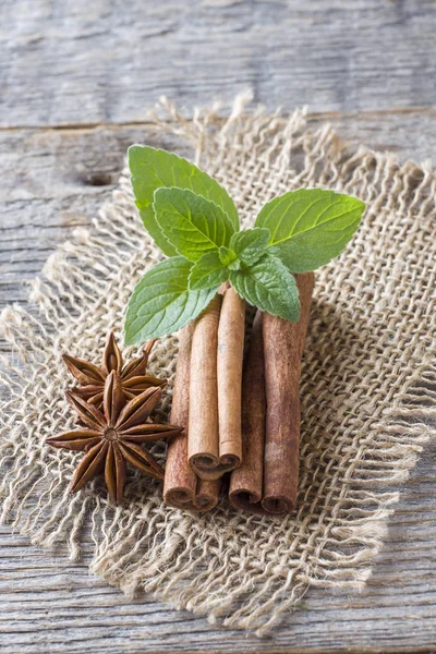 Cinnamon sticks and anise stars with mint on wooden background. Fragrant Oriental spice.