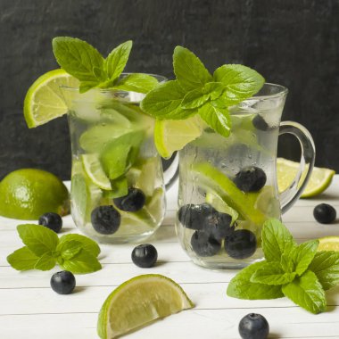 Serinletici içecekler limonata yaz ya da kireç taze nane yaban mersini buzla kokteyl Mojito. Masa lambası, karanlık duvar.