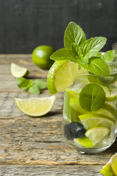 Serinletici içecekler limonata yaz ya da kireç taze nane yaban mersini buzla kokteyl Mojito. Ahşap arka plan.