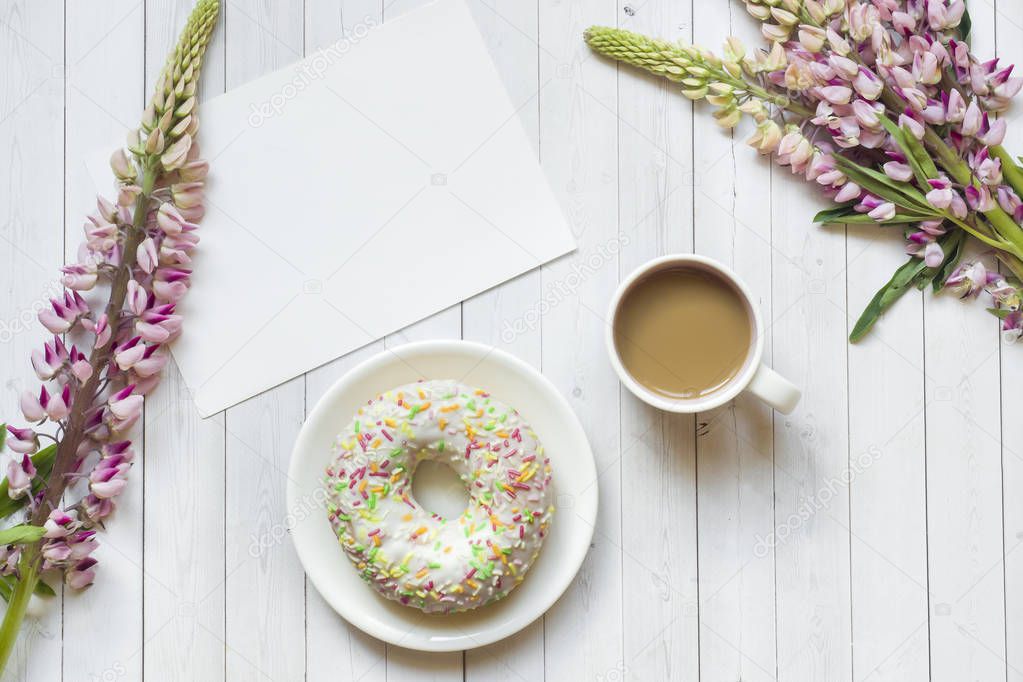 Still life with a Cup of coffee and lupine flowers donut on a light wooden table