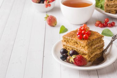 Tatlım kek çilek, nane ve Frenk üzümü, bir fincan çay hafif bir arka plan üzerinde.