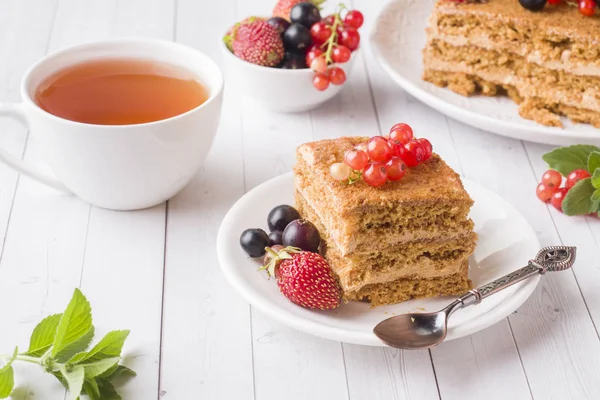 Tatlım kek çilek, nane ve Frenk üzümü, bir fincan çay hafif bir arka plan üzerinde.