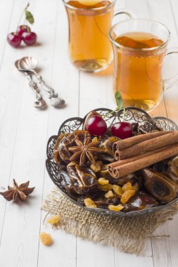 Oryantal tatlılar, kurutulmuş meyve tarihleri ve kuru üzüm, tarçın ve anasonu bir tabak içinde. Ahşap arka plan üzerinde bardaklarda Türk çayı