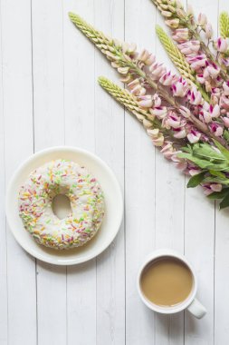Bir fincan kahve ve acı bakla çiçek çörek üzerinde ahşap masa lambası ile natürmort
